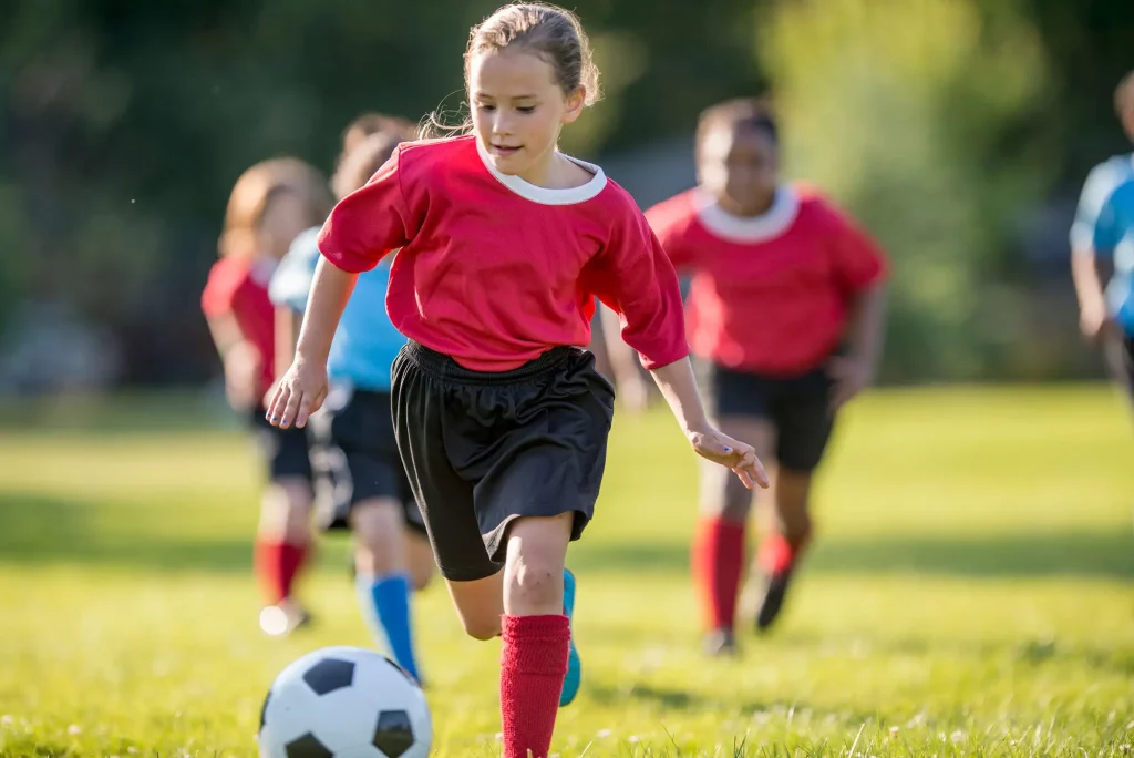 Children in light blue and red uniforms playing in a game of soccer